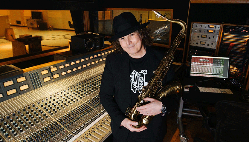 Boney James In Black Clothes And Hat Holding A Saxophone By A Soundboard