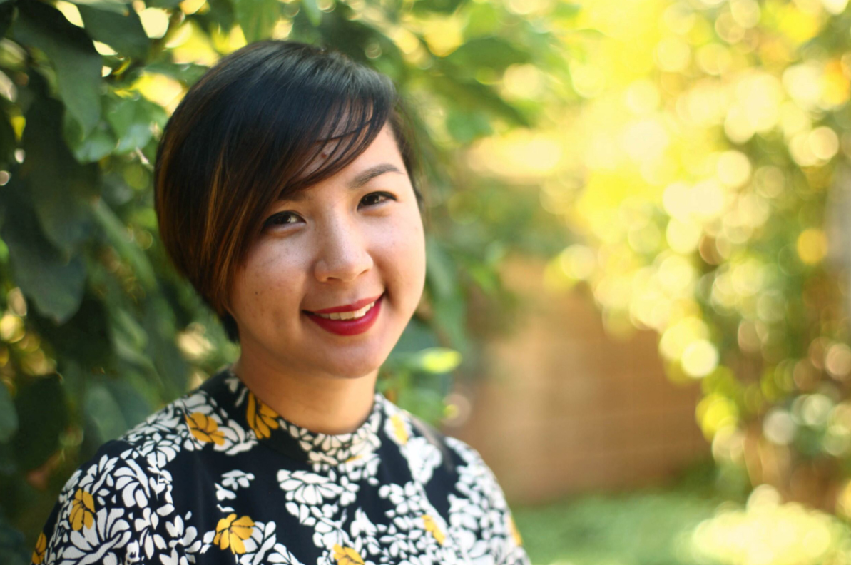 Cathy Linh Che Wearing A Floral Shirt Outside Under A Tree With A Fence In The Background