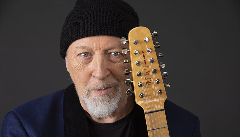 Richard Thompson Wearing A Blue Blazer And Black Beanie And Holding His Guitar