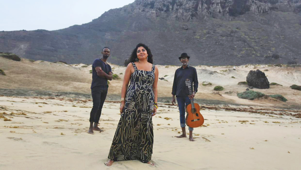 Kativa Shah On A Beach With Musicians And Mountains In Background