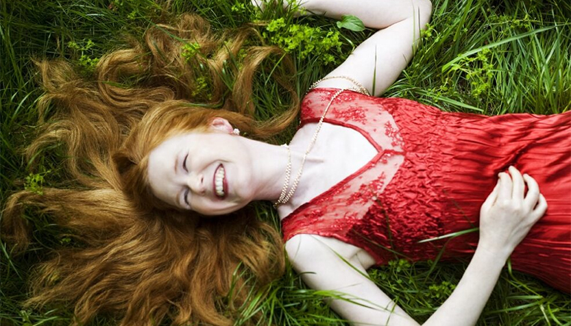 Sarah Cahill Wearing A Red Dress And Laying With Her Hair Spread Over The Grass