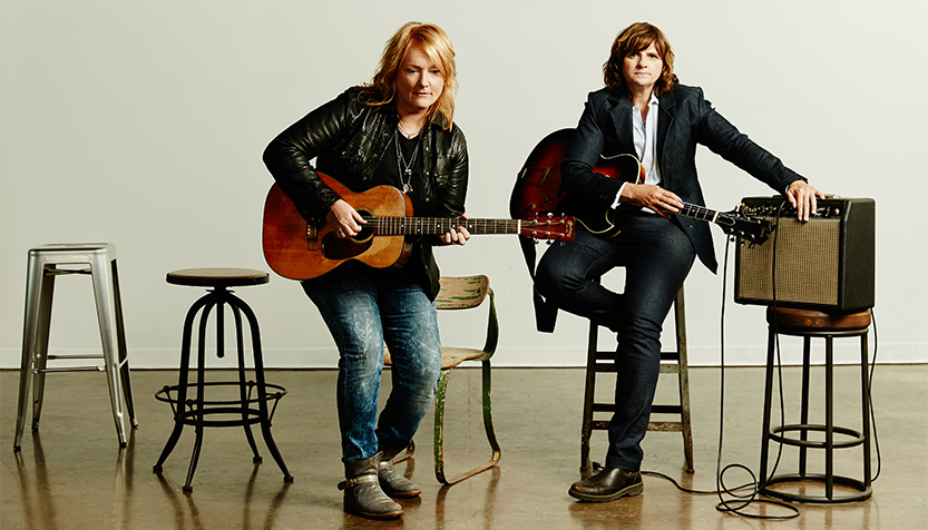 Indigo Girls Wearing Black Jackets And Jeans And Holding Their Guitars