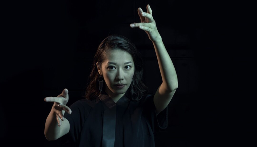 Miho Hazama Conducting In A Black Shirt Against A Black Background