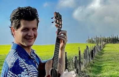 Jeff Peterson Playing His Ukulele By A Fence In A Field