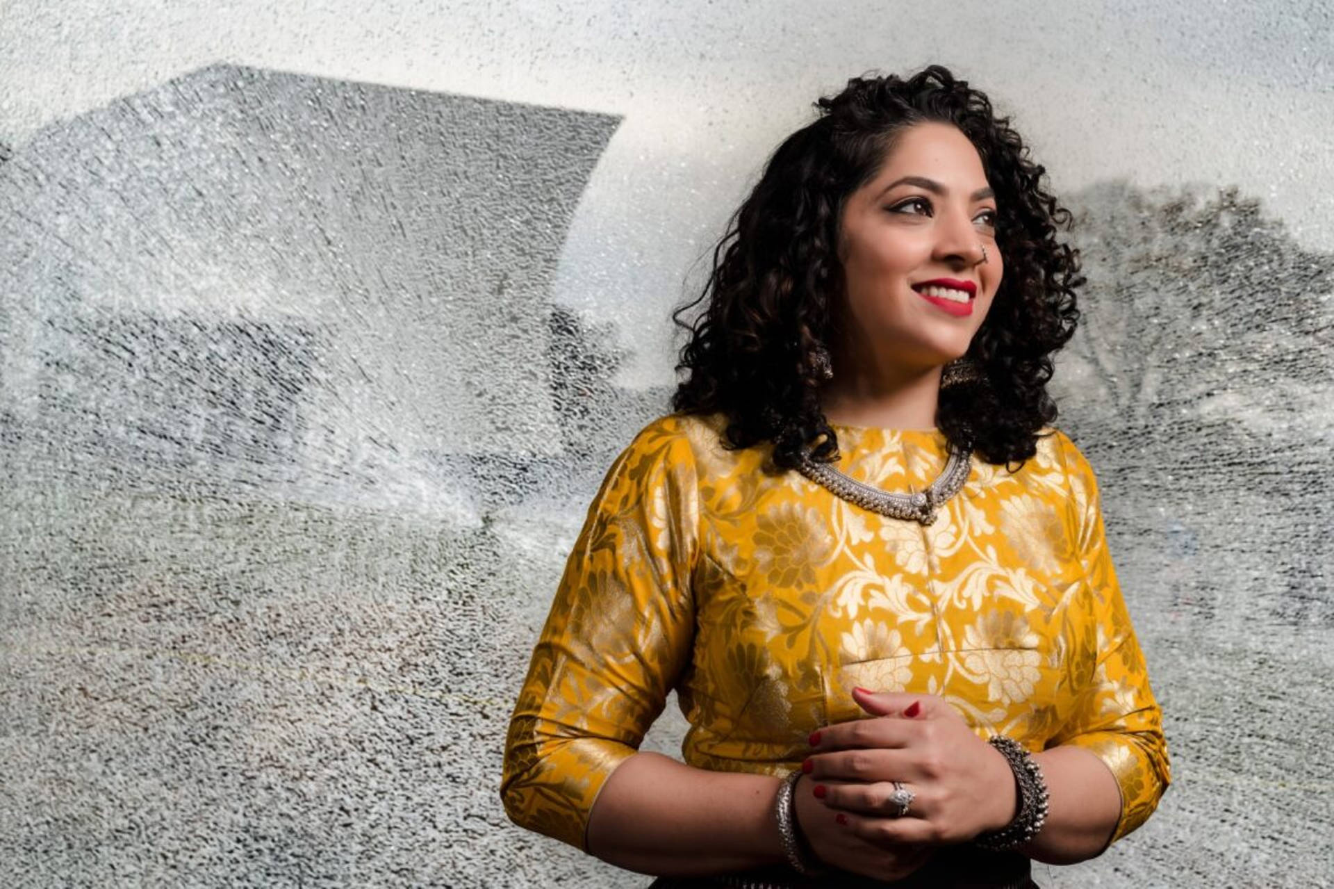 Nistha Raj Wearing A Yellow And Gold Tunic In Front Of A Gray Background